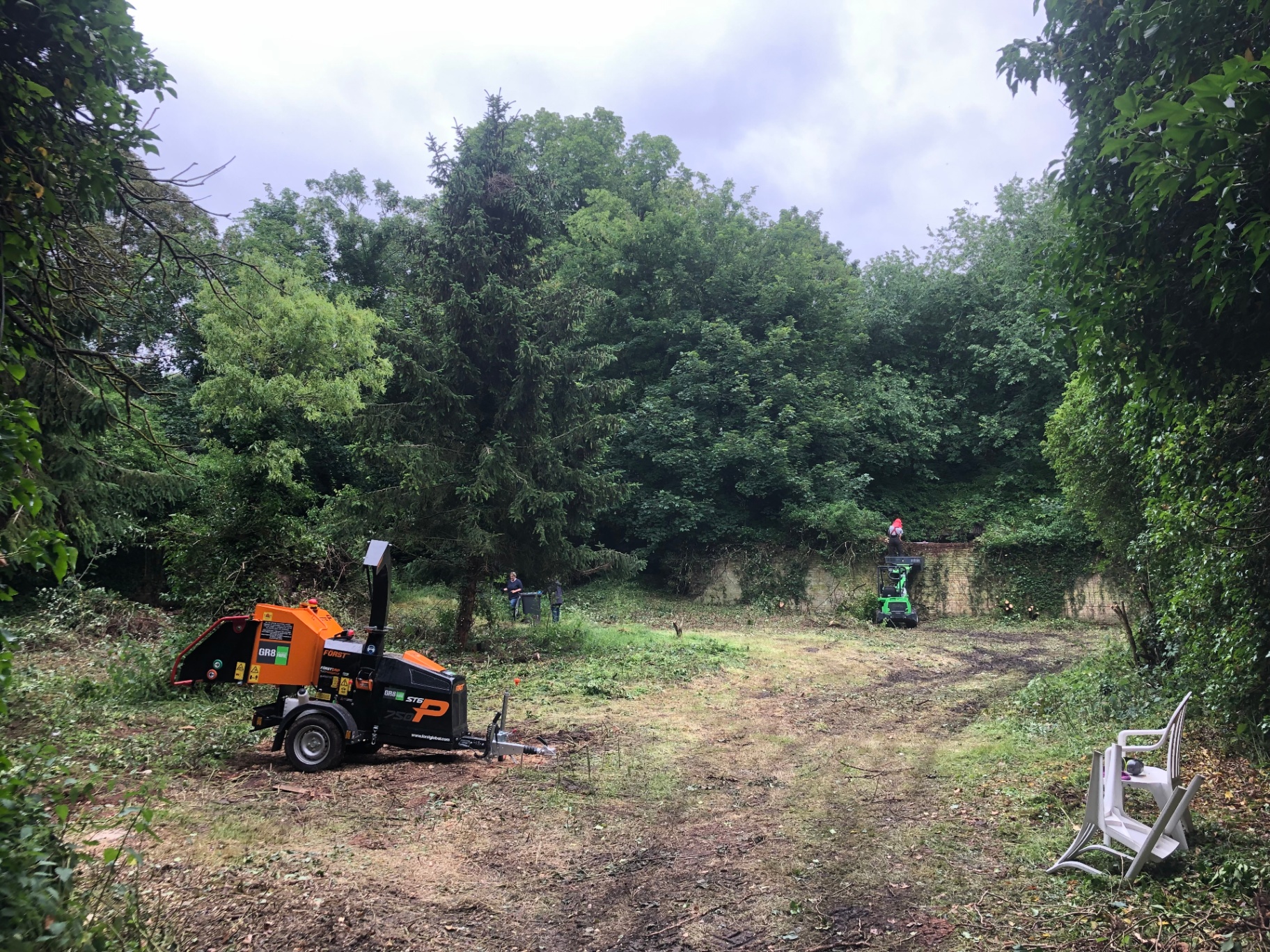 The courtyard mid-clearing, with a wood chipper and small loader working through cut branches